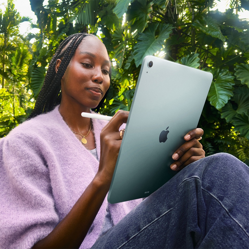 Mujer sentada en un entorno natural usando el iPad Air azul con el Apple Pencil, mientras dibuja o escribe sobre la pantalla.